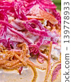 Sliced carrots and onions prepare with creamy sauce at a food stall in a bustling market during the day. People gather around to enjoy the dish 139778933