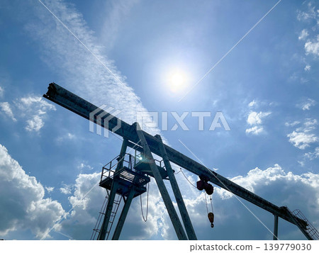 Industrial gantry crane silhouette against bright sun and blue sky at cargo loading facility Industrial gantry crane silhouette against bright sun and blue sky at cargo loading facility 139779030