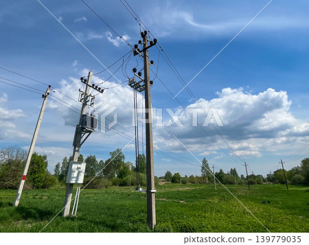 Rural electricity transmission lines and utility poles across green landscape under cloudy sky Rural electricity transmission lines and utility poles across green landscape under cloudy sky 139779035