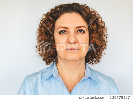 Serious mature woman with curly hair wearing blue shirt portrait for business and professional use Serious mature woman with curly hair wearing blue shirt portrait for business and professional use 139779127