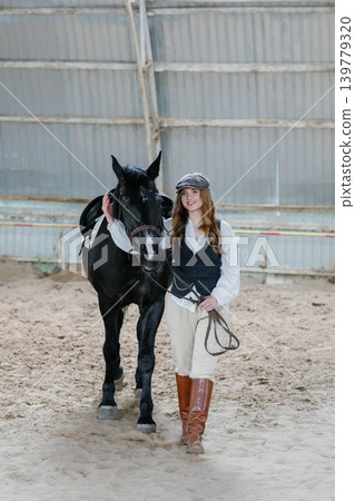 Woman rider posing with her horse in an arena Woman rider posing with her horse in an arena 139779320