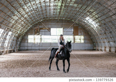 Woman riding horse in indoor equestrian arena Woman riding horse in indoor equestrian arena 139779326