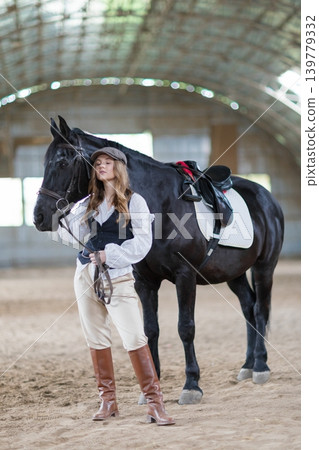 Woman with flat cap and black horse in riding arena Woman with flat cap and black horse in riding arena 139779332