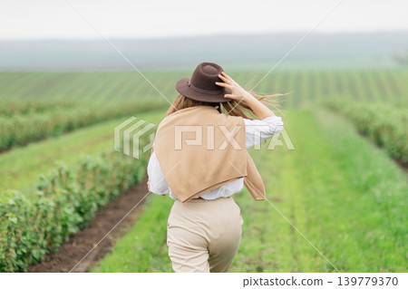 Woman walking through green agricultural field wearing a hat 139779370