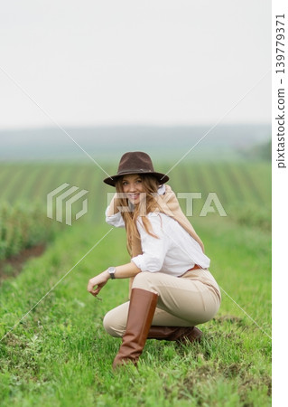 Woman smiling wearing hat and boots in field Woman smiling wearing hat and boots in field 139779371