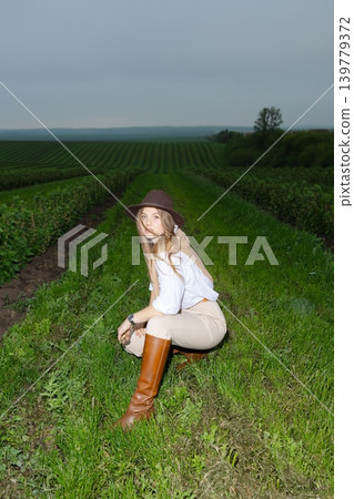 Woman smiling wearing hat and boots in field Woman smiling wearing hat and boots in field 139779372
