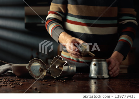 A man in a striped jumper is about to make coffee in an old Italian coffee maker. A man in a striped jumper is about to make coffee in an old Italian coffee maker. 139779435