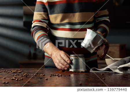 A man in a striped jumper is about to make coffee in an old Italian coffee maker. 139779440