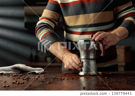 A man in a striped jumper is about to make coffee in an old Italian coffee maker. A man in a striped jumper is about to make coffee in an old Italian coffee maker. 139779441
