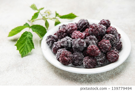 Frozen blackberries on white plate with fresh leaves Frozen blackberries on white plate with fresh leaves 139779494