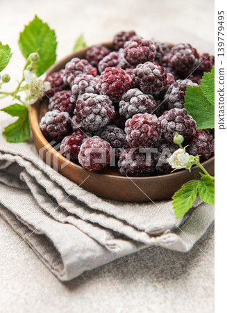 Frozen blackberries with green leaves in wooden bowl Frozen blackberries with green leaves in wooden bowl 139779495
