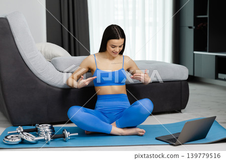 Young woman doing home workout training with laptop Young woman doing home workout training with laptop 139779516