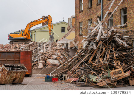 Excavator demolishing old brick building with large piles of construction debris and timber waste Excavator demolishing old brick building with large piles of construction debris and timber waste 139779824