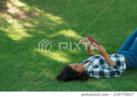 Woman, knowledge and reading book on grass, literature and smiling for fiction or fantasy story. Female person, nature and relaxing on lawn for education, information and student studying in garden Woman, knowledge and reading book on grass, literature and smiling for fiction or fantasy story. Female person, nature and relaxing on lawn for education, information and student studying in garden 139779857