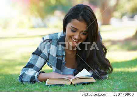 Woman, novel and reading book on grass, literature and smiling for fiction or fantasy story. Happy female person, nature and relaxing on lawn for knowledge, education and student studying in garden 139779909