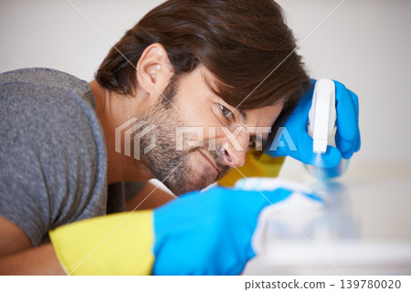 Man, face and spraying surface for housekeeping, hygiene or disinfection on furniture or table at home. Male person, maid or cleaner checking dirty spots for wiping, bacteria or germ removal at house Man, face and spraying surface for housekeeping, hygiene or disinfection on furniture or table at home. Male person, maid or cleaner checking dirty spots for wiping, bacteria or germ removal at house 139780020