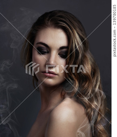 Woman, eyeshadow and makeup, beauty and smoke with hair, cosmetics and balayage on grey background. Serious model, edgy with haircare and vapor, cosmetology and skin with mist or fog in studio Woman, eyeshadow and makeup, beauty and smoke with hair, cosmetics and balayage on grey background. Serious model, edgy with haircare and vapor, cosmetology and skin with mist or fog in studio 139780185