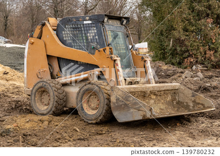 Bobcat excavator performs earthmoving tasks at a construction site on a cold winter day in a rural setting with surrounding trees Bobcat excavator performs earthmoving tasks at a construction site on a cold winter day in a rural setting with surrounding trees 139780232