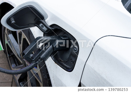 Charger is plugged into an electric car providing energy to the vehicle at a charging station in the morning light Charger is plugged into an electric car providing energy to the vehicle at a charging station in the morning light 139780253