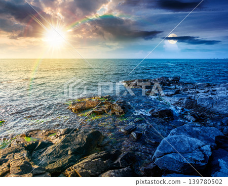 day meet night. sea coast with stones and boulders. view of beach with rock in seaweed. sun and moon on epic sky above horizon. autumn equinox harmony concept for astrology background day meet night. sea coast with stones and boulders. view of beach with rock in seaweed. sun and moon on epic sky above horizon. autumn equinox harmony concept for astrology background 139780502