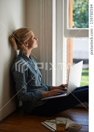 Woman, freelancer and laptop by window, writer and internet connection on floor for info. Female person, editor and website for research or online news, blogging and typing an article on technology 139780594