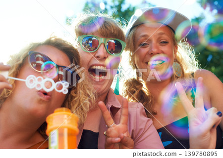 Women, friends and bubbles for blowing or happy outdoor with sunglasses or peace sign for holiday and relax. People, face and plastic wand or toy for playing and laughing with vacation or adventure Women, friends and bubbles for blowing or happy outdoor with sunglasses or peace sign for holiday and relax. People, face and plastic wand or toy for playing and laughing with vacation or adventure 139780895
