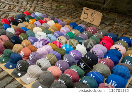 New york, usa august 18,2024. Row of colorful nyc baseball caps with ny and new york logos on cobblestone street at a souvenir vendor, 5 sale sign visible New york, usa august 18,2024. Row of colorful nyc baseball caps with ny and new york logos on cobblestone street at a souvenir vendor, 5 sale sign visible 139781383