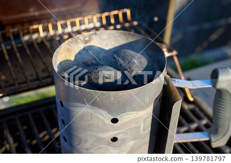 Metal charcoal chimney filled with charcoal releases smoke on outdoor grill Metal charcoal chimney filled with charcoal releases smoke on outdoor grill 139781797