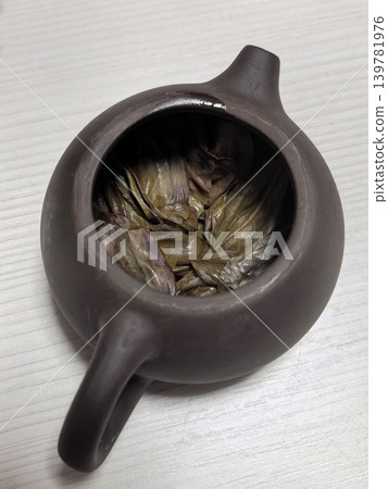 Unique clay teapot filled with green tea leaves for a delightful brew Unique clay teapot filled with green tea leaves for a delightful brew 139781976