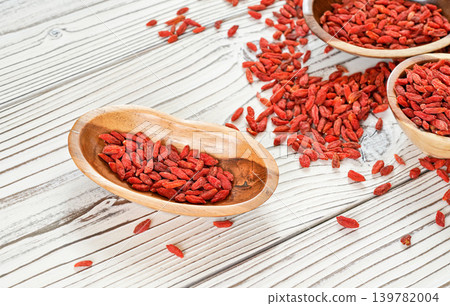 Dried goji aka. wolfberry seeds in wooden bowls and spilled on white boards desk Dried goji aka. wolfberry seeds in wooden bowls and spilled on white boards desk 139782004