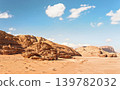 Rocky massifs on red sand desert, vehicle tracks ground, bright cloudy sky in background, typical scenery in Wadi Rum, Jordan 139782032