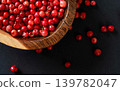 Whole pink / red peppercorns in small wooden bowl, some scattered on black / gray paper, closeup view from above 139782047