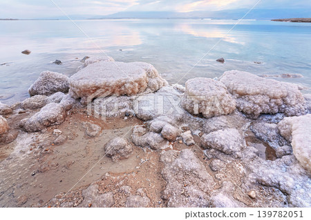 Sand and stones covered with crystalline salt on shore of Dead Sea, clear water background - typical morning scenery at Ein Bokek beach, Israel Sand and stones covered with crystalline salt on shore of Dead Sea, clear water background - typical morning scenery at Ein Bokek beach, Israel 139782051
