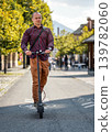 Young man in trousers and shirt, bag over his shoulder, riding electric scooter towards camera 139782060