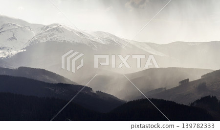 Breathtaking view of magnificent foggy Carpathian mountains, covered with ever-green forest on misty quiet morning or evening under dark cloudy sky. Mountains tops covered with snow in distance. Breathtaking view of magnificent foggy Carpathian mountains, covered with ever-green forest on misty quiet morning or evening under dark cloudy sky. Mountains tops covered with snow in distance. 139782333