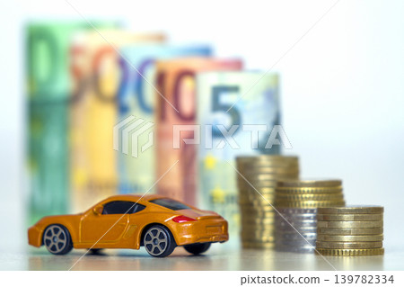 Blurred row of rolled hundred, fifty, twenty, ten and five new euro banknotes and pile of coins with yellow toy expensive sport car. Symbol of financial prosperity, vehicle sale and purchase. Blurred row of rolled hundred, fifty, twenty, ten and five new euro banknotes and pile of coins with yellow toy expensive sport car. Symbol of financial prosperity, vehicle sale and purchase. 139782334