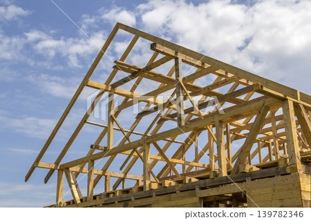 New wooden ecological house from natural materials under construction. Close-up detail of attic roof frame against clear sky. Building, roofing, construction and renovation concept. New wooden ecological house from natural materials under construction. Close-up detail of attic roof frame against clear sky. Building, roofing, construction and renovation concept. 139782346