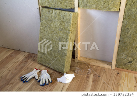 Rock wool and fiberglass insulation staff material for cold barrier. Tools for work with glass wool: protective goggles, glasses and mask. Warm home, economy, construction and renovation concept. Rock wool and fiberglass insulation staff material for cold barrier. Tools for work with glass wool: protective goggles, glasses and mask. Warm home, economy, construction and renovation concept. 139782354