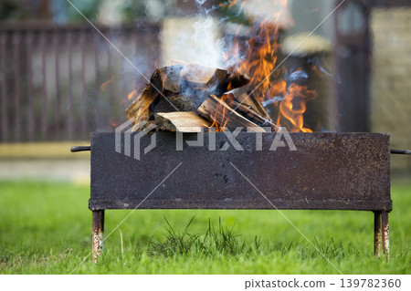 Brightly burning in metal box firewood for barbecue outdoor. Camping, safety and tourism concept. Brightly burning in metal box firewood for barbecue outdoor. Camping, safety and tourism concept. 139782360