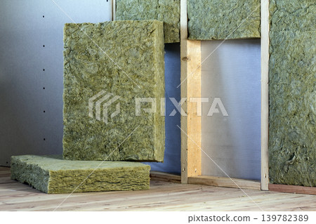 Wooden frame for future walls with drywall plates insulated with rock wool and fiberglass insulation staff for cold barrier. Comfortable warm home, economy, construction and renovation concept. Wooden frame for future walls with drywall plates insulated with rock wool and fiberglass insulation staff for cold barrier. Comfortable warm home, economy, construction and renovation concept. 139782389