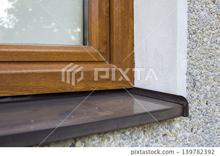 Close-up detail of white plastered house wall with newly installed new brown plastic window and metal windowsill. Modern technology, warm and comfortable home, professional job concept. Close-up detail of white plastered house wall with newly installed new brown plastic window and metal windowsill. Modern technology, warm and comfortable home, professional job concept. 139782392