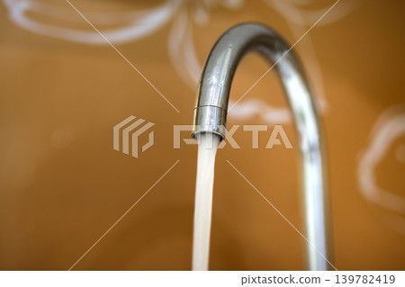 Water tap, chrome stainless metal faucet with running stream of water in bathroom or kitchen, mixer cold hot water isolated on bright yellow copy space background. Modern kitchen interior. Water tap, chrome stainless metal faucet with running stream of water in bathroom or kitchen, mixer cold hot water isolated on bright yellow copy space background. Modern kitchen interior. 139782419