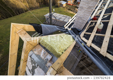Roof construction and insulation with mineral wool. Wooden beams frame on walls of hollow foam insulation blocks. Roofing underlayment, water-resistant waterproof barrier material as protection. Roof construction and insulation with mineral wool. Wooden beams frame on walls of hollow foam insulation blocks. Roofing underlayment, water-resistant waterproof barrier material as protection. 139782428