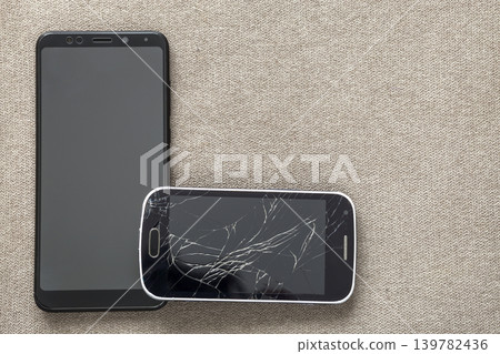 Comparison of two black mobile phones, old cellphone with cracked screen and new modern on light cloth copy space background. Technology progress and replacement concept. 139782436