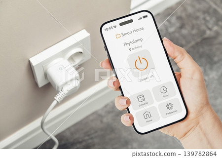 Female hand holding smartphone with smart home application interface for controlling a smart socket Female hand holding smartphone with smart home application interface for controlling a smart socket 139782864