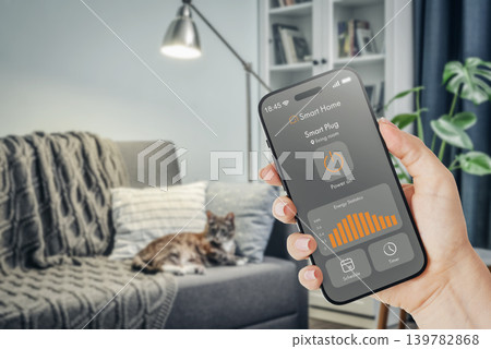 Female hand holding smartphone with smart home application interface showing energy monitoring statistics Female hand holding smartphone with smart home application interface showing energy monitoring statistics 139782868