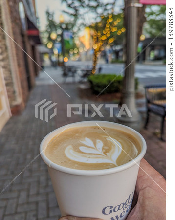 Hand Holding Takeaway Coffee Cup with Latte Art on Urban Street with Soft Bokeh Lights Background Hand Holding Takeaway Coffee Cup with Latte Art on Urban Street with Soft Bokeh Lights Background 139783343