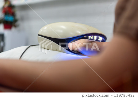 Closeup of hand under UV nail lamp during manicure treatment in beauty salon highlighting nail care grooming cosmetic technology 139783452