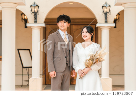Bride and groom in a dress holding dried flowers and swags in the wedding chapel Bride and groom in a dress holding dried flowers and swags in the wedding chapel 139783807