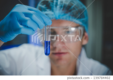 Male scientist holding test tube with blue chemical solution inside advanced laboratory for research in biology, chemistry, and medical study Male scientist holding test tube with blue chemical solution inside advanced laboratory for research in biology, chemistry, and medical study 139784402